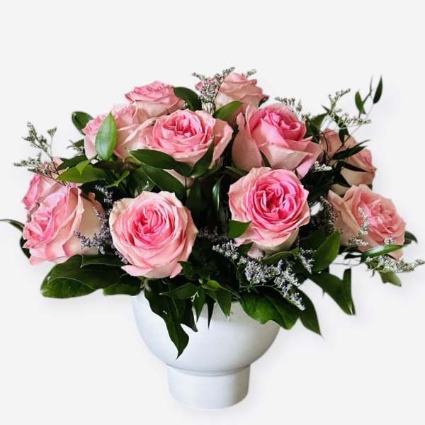 Pink roses arranged in a white vase with greenery