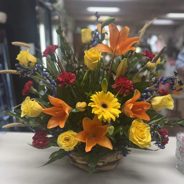 Mixed bouquet with orange lilies, yellow roses, and a yellow gerbera daisy in a basket