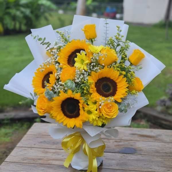 Bouquet of sunflowers and yellow roses wrapped in white paper with a yellow ribbon
