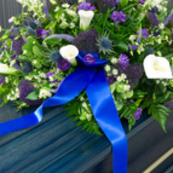 Purple and white floral spray on a casket with a blue ribbon