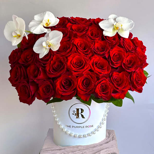 Round box arrangement of red roses with white orchids on a white hatbox with pearl trim