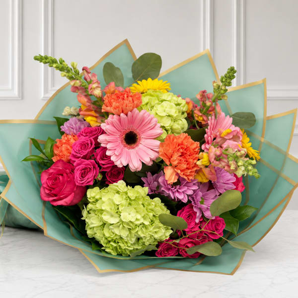 Mixed bouquet of pink, orange, yellow, and green flowers wrapped in teal paper