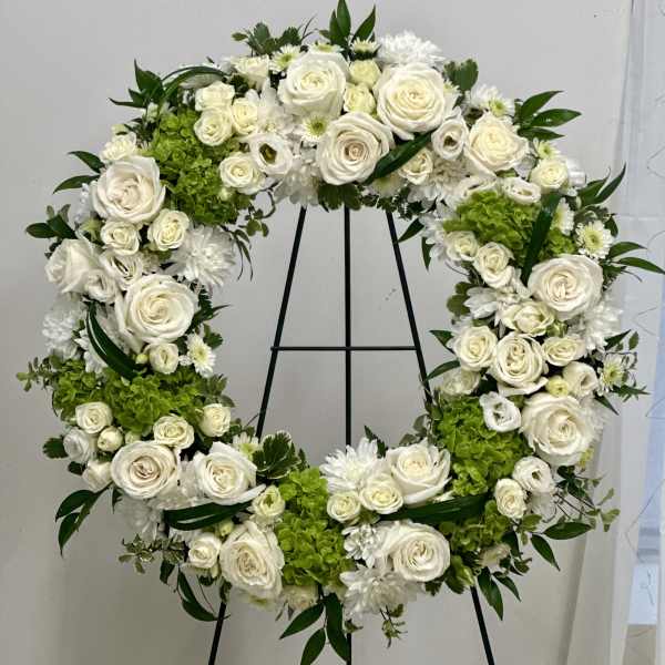 White floral wreath on a black stand with green accents