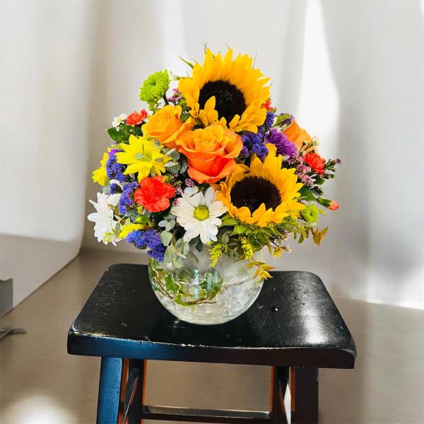 Mixed bouquet with sunflowers, orange roses, and daisies in a glass vase