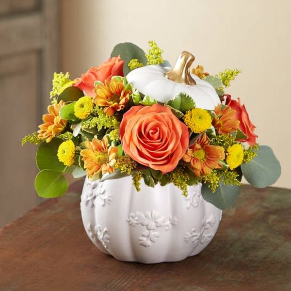 Orange roses and yellow flowers arranged in a white pumpkin vase