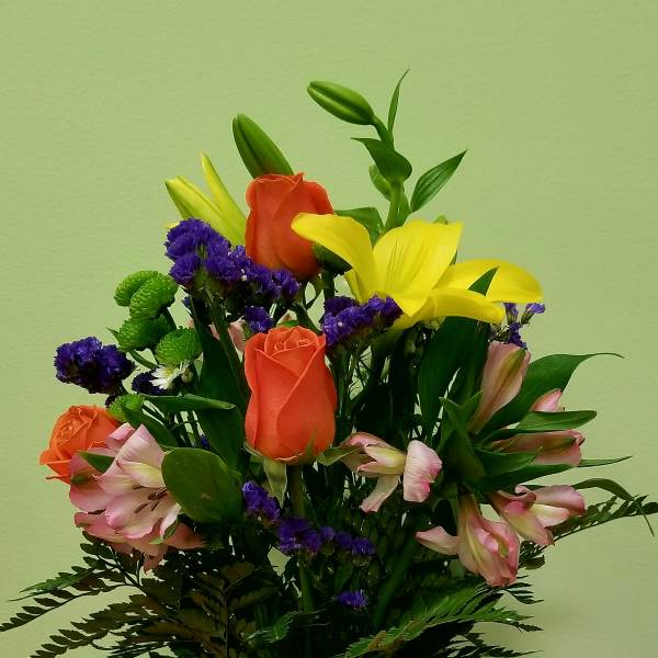 Mixed bouquet of lilies, roses, and purple filler flowers in a glass vase