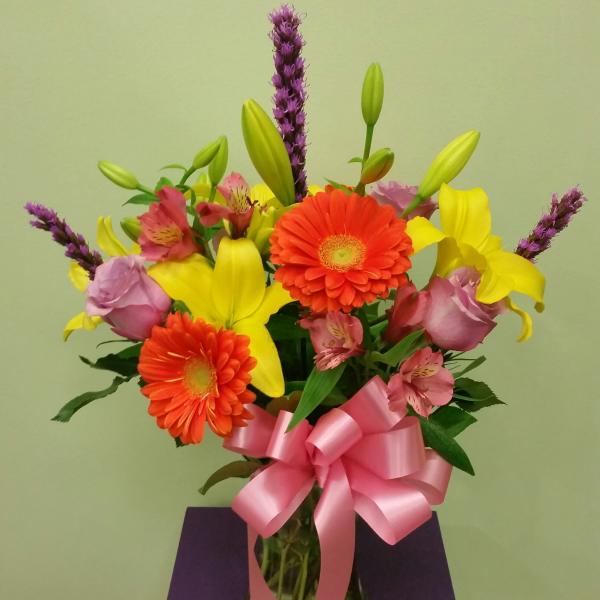 Bouquet of yellow lilies, orange gerberas, and pink roses in a glass vase