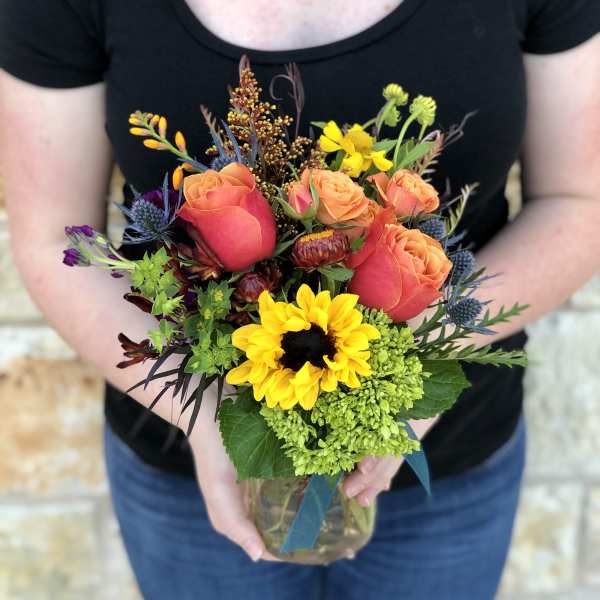 Mixed bouquet of orange roses, sunflowers, and green hydrangea in a glass vase