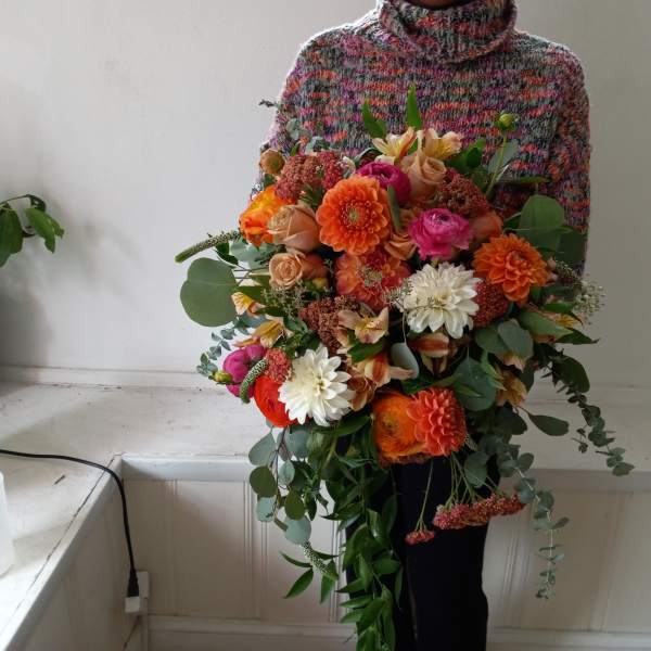 Person holding a large bouquet of orange, pink, and white flowers