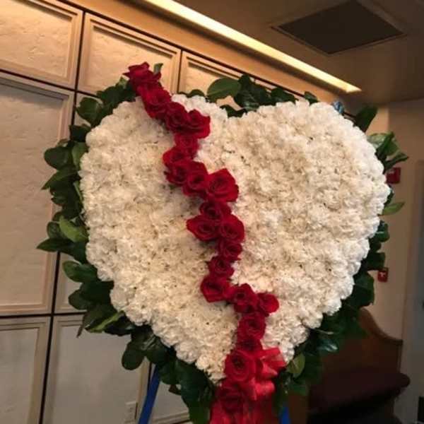 Heart-shaped white floral wreath with a red rose ribbon and green border