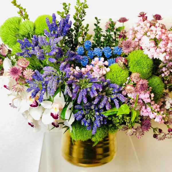 Mixed bouquet with purple, pink, white, and green flowers in a gold vase