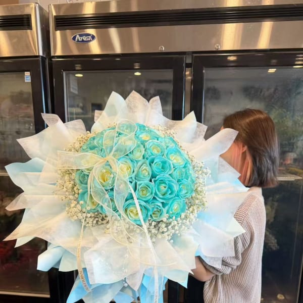 Large turquoise rose bouquet wrapped in white paper with a ribbon