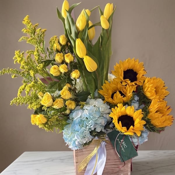Yellow tulips, roses, sunflowers, and blue hydrangeas in a wooden box