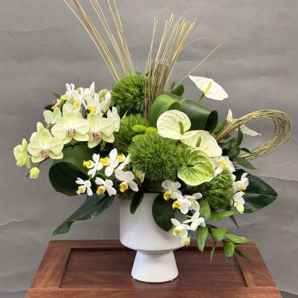 White and green floral arrangement in a white pedestal vase