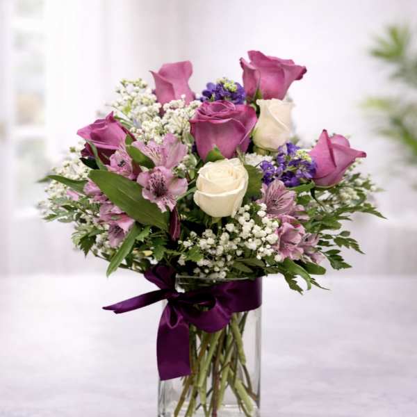 Bouquet of purple and white roses in a clear glass vase with a ribbon