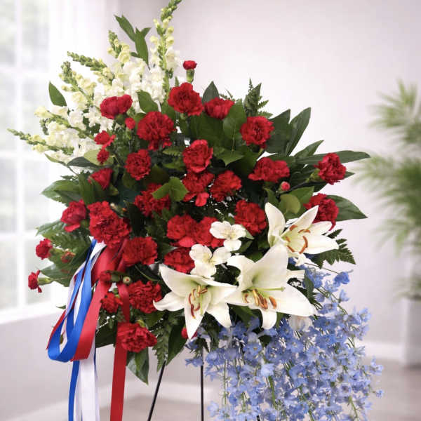 Standing floral spray with red carnations, white lilies, and blue flowers on a tripod easel