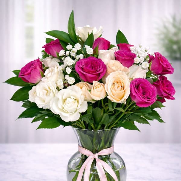 Bouquet of pink, white, and peach roses in a clear glass vase with a ribbon