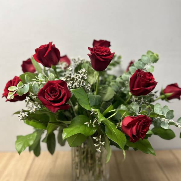 Red roses arranged in a clear glass vase with greenery