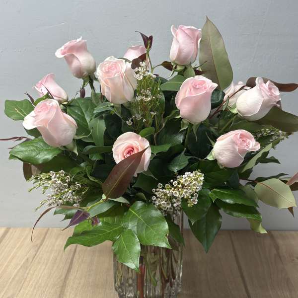 Pink roses arranged in a clear glass vase with greenery