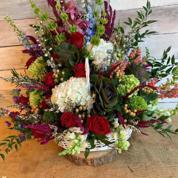 Large mixed flower arrangement with red roses, white hydrangea, and purple accents in a white basket