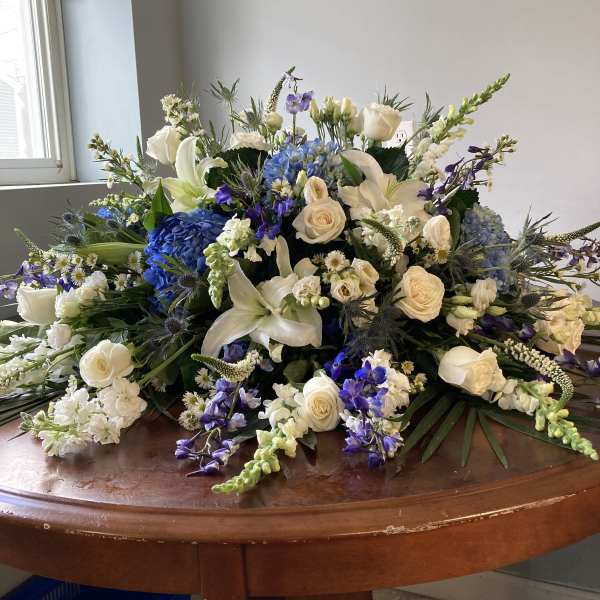 Large floral arrangement with white roses, lilies, and blue blooms on a table