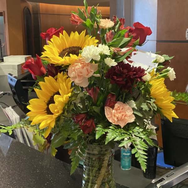 Mixed bouquet with sunflowers, roses, carnations, and alstroemeria in a glass vase