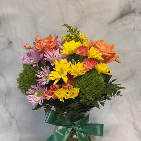 Mixed bouquet of orange roses, yellow daisies, and purple flowers in a glass vase