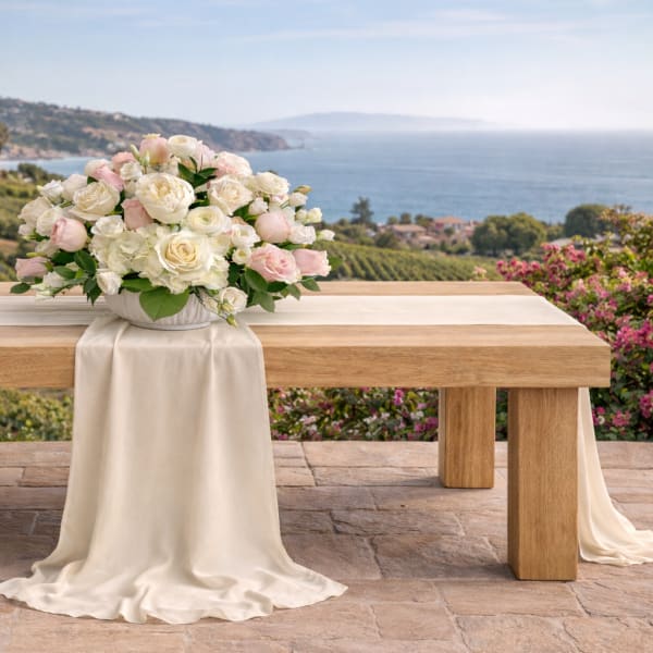 White and blush rose arrangement on a draped table outdoors