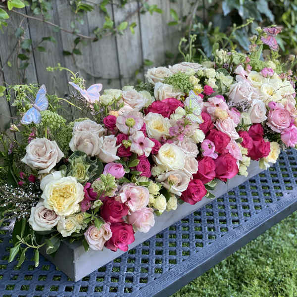 Long floral centerpiece of pink and cream roses with butterfly accents