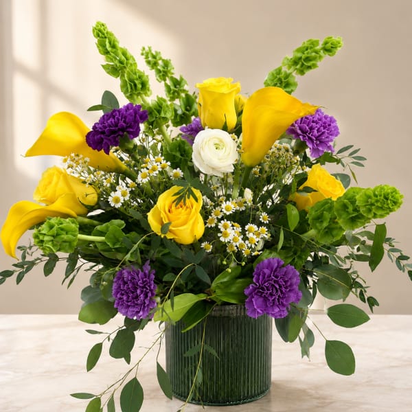 Bouquet of yellow roses, purple carnations, and white daisies in a glass vase
