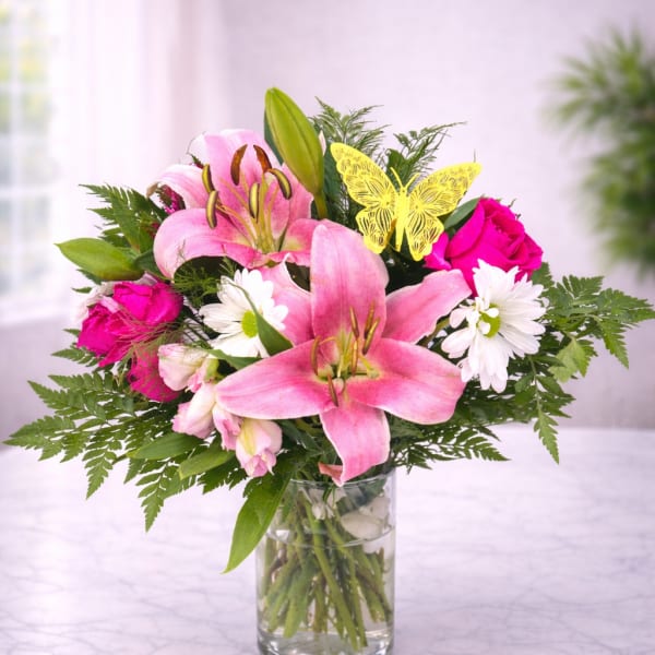 Pink lilies and roses arranged in a clear glass vase