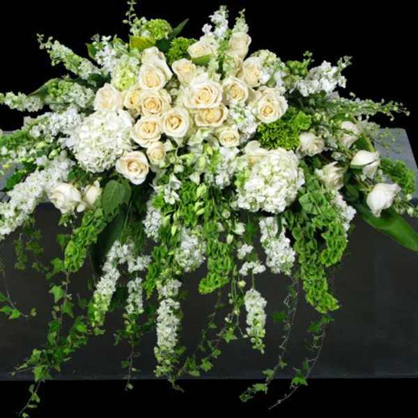White rose and hydrangea arrangement with trailing greenery on a dark pedestal
