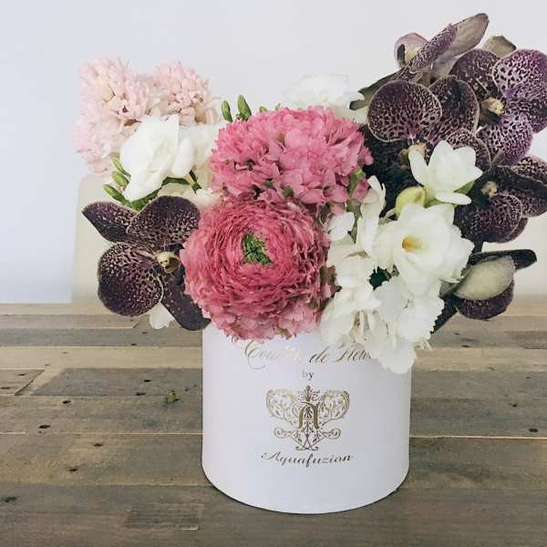 Pink and white floral arrangement in a white hatbox with dark orchids