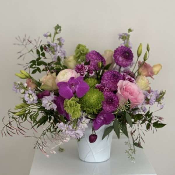 Mixed pink, purple, and green flowers arranged in a white vase