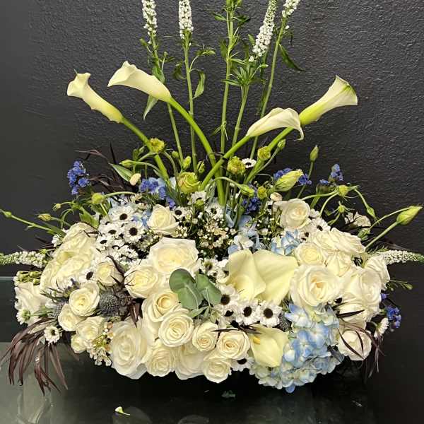 Large white floral arrangement with calla lilies, roses, and blue hydrangeas