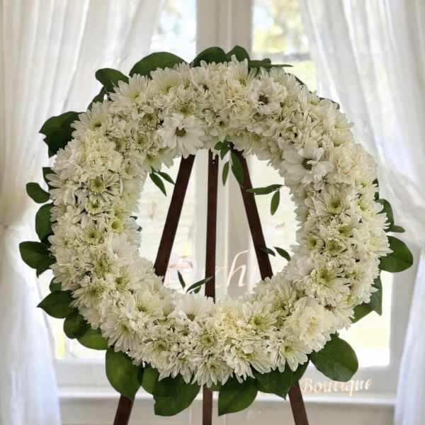 White flower wreath on a wooden easel with green leaves