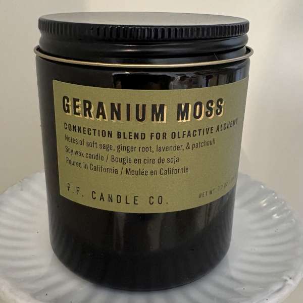 Black jar candle with a tan label on a white pedestal