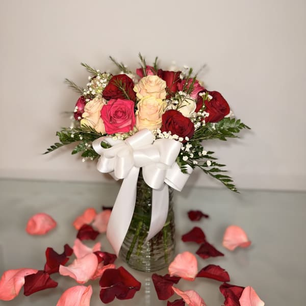 Bouquet of red, pink, and cream roses in a glass vase with a white ribbon