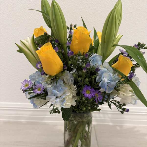 Bouquet of yellow roses, blue hydrangeas, and purple daisies in a glass vase