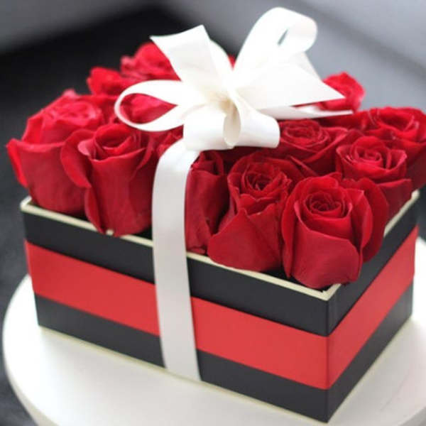 Red roses arranged in a black and red gift box with a white ribbon bow