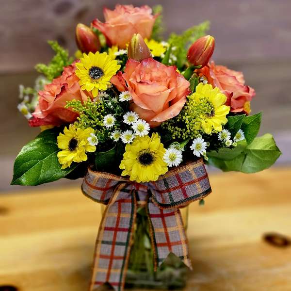 Bouquet of peach roses and yellow daisies in a glass vase with a plaid ribbon