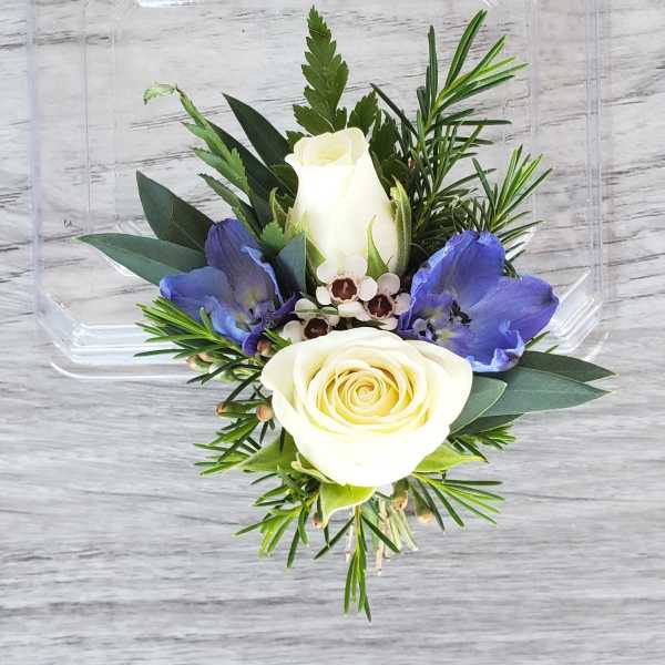 White rose boutonniere with blue flowers and greenery