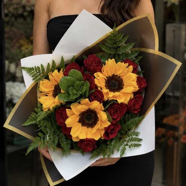Bouquet of red roses and yellow sunflowers wrapped in white and brown paper