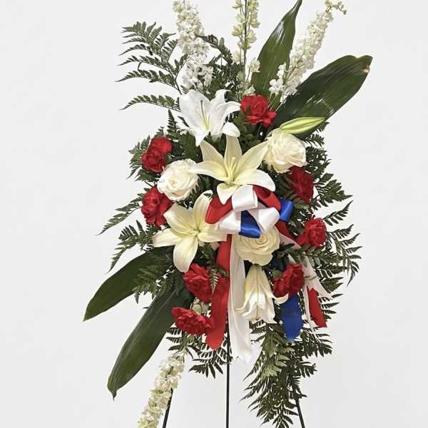 Standing floral spray with red and white flowers and ribbon on a black easel