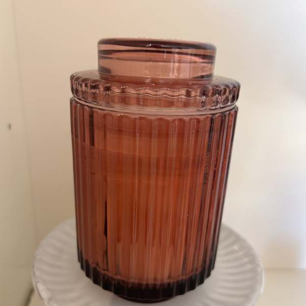 Amber glass jar candle with a matching lid on a white pedestal