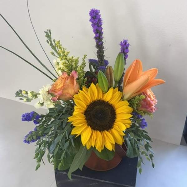 Sunflower arrangement with orange lilies and purple accents in a vase