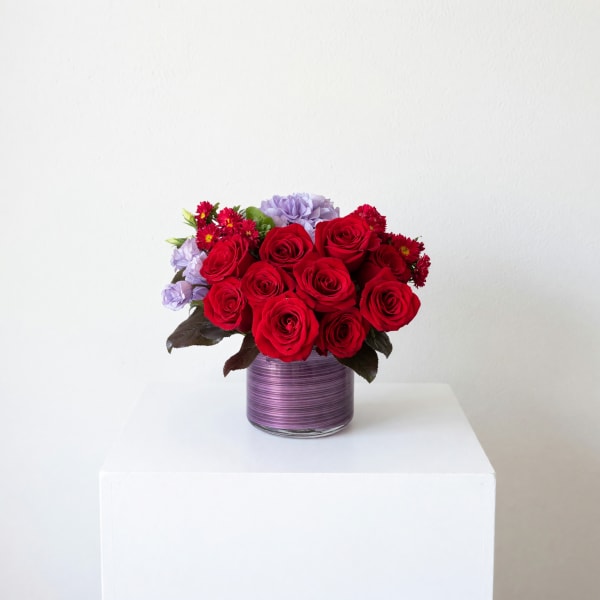 Red roses and lavender flowers in a purple glass vase
