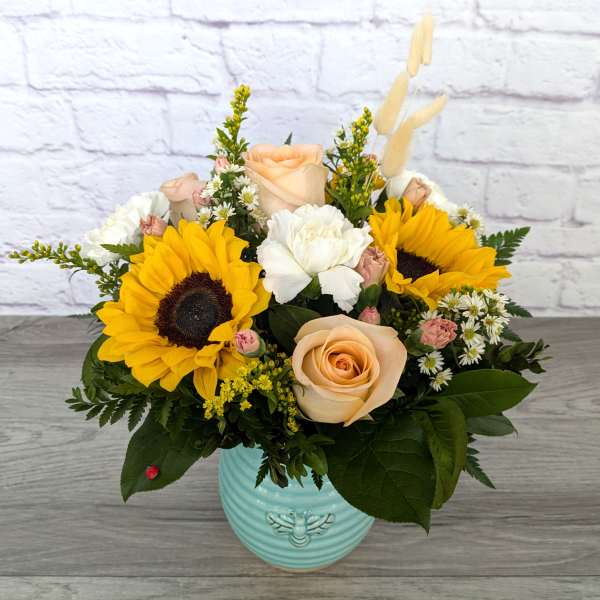 Mixed bouquet with sunflowers, roses, and white blooms in a blue vase