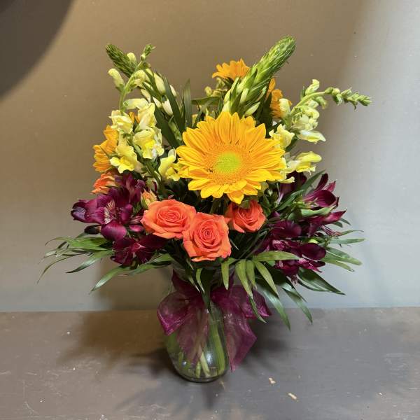 Mixed bouquet with orange roses, yellow daisies, and purple flowers in a glass vase