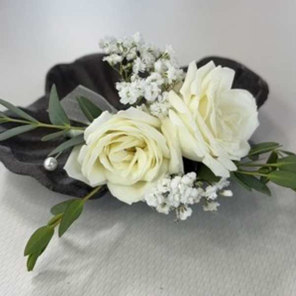 White rose boutonniere with small white filler flowers and dark green leaves